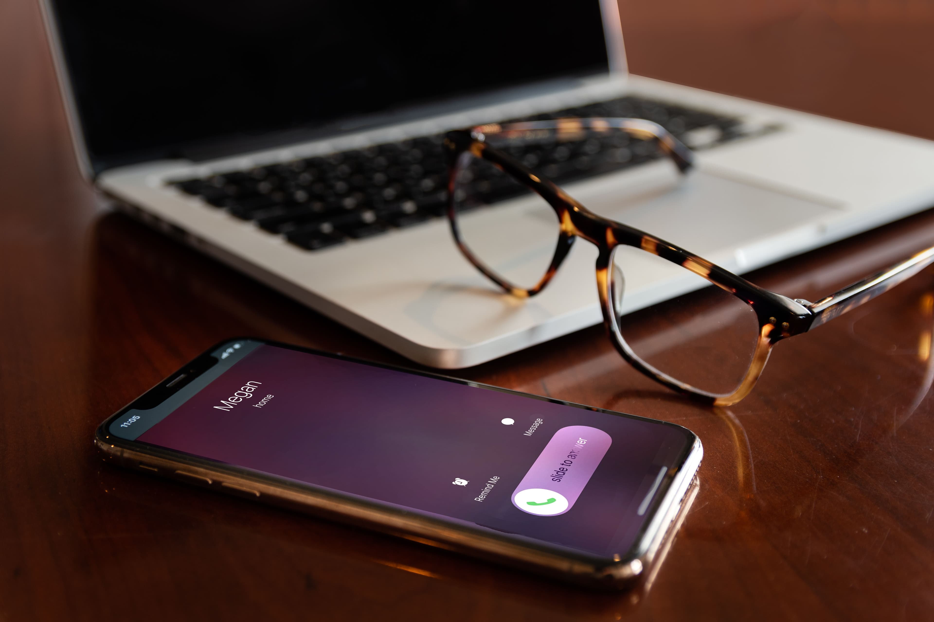 A smartphone with an incoming call next to a laptop on a desk.